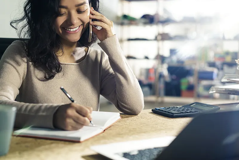 Woman smiling while talking on the phone and taking notes